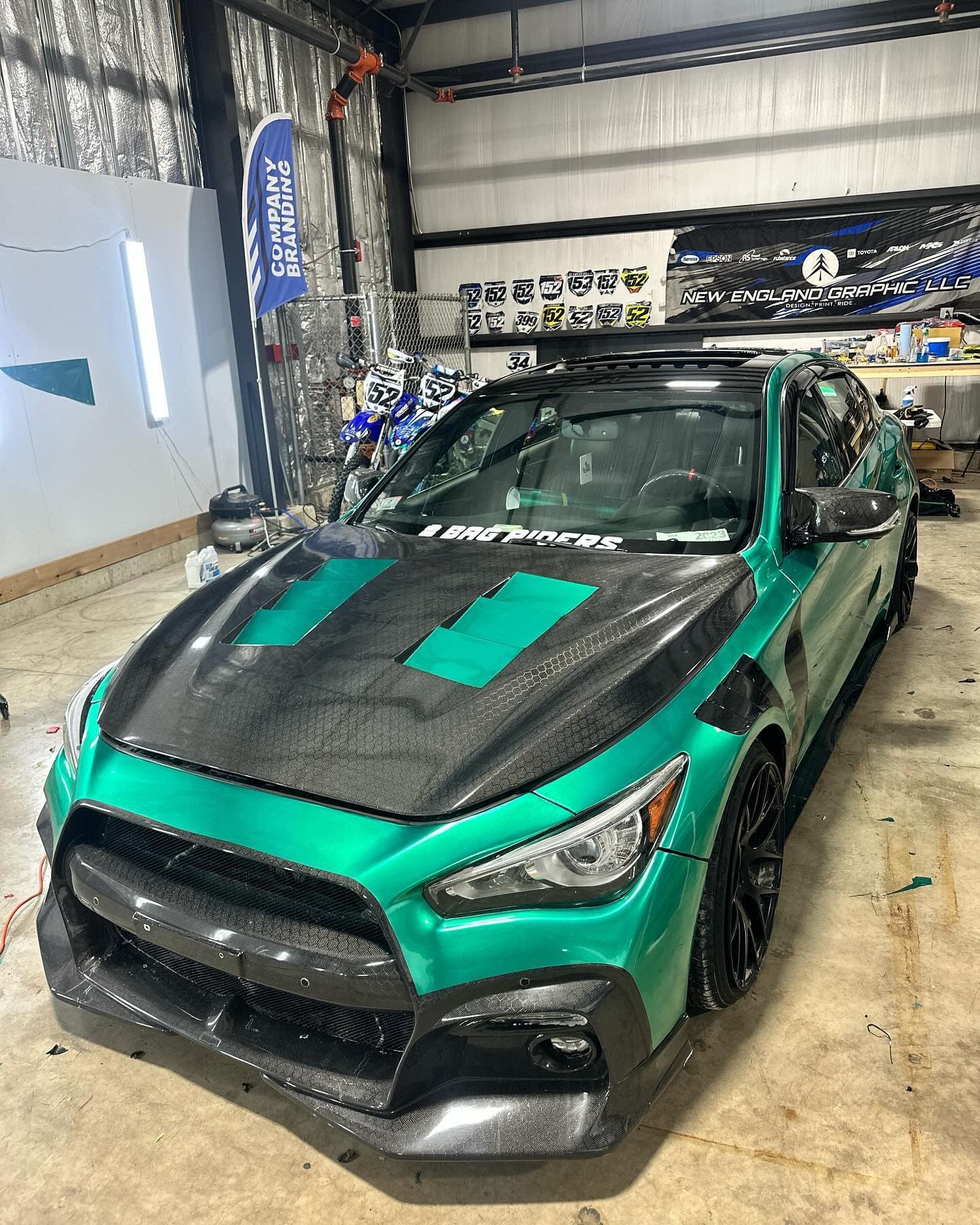 Green Infiniti Q50 with a carbon hood and custom graphics, inside the shop.